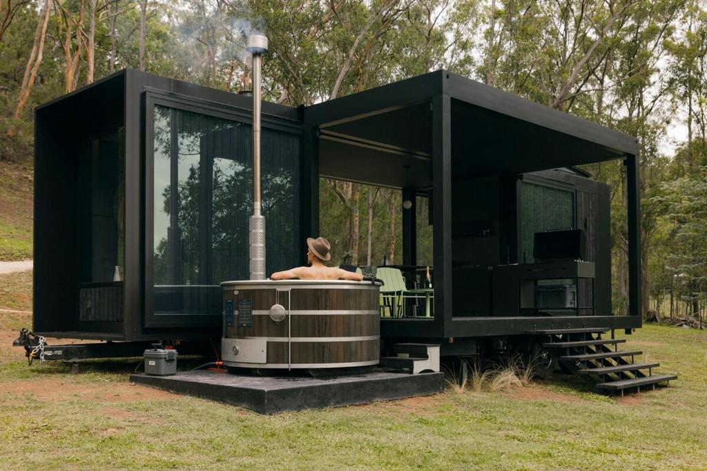 a black tiny house with a person sitting in a hot tub at The Lookout - a Huch experience in Wollombi