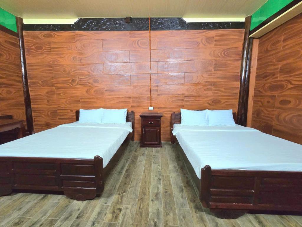Làng Du Lịch Sinh Thái Đá Nổi في Phong Ðiền: سريرين في غرفة ذات جدران خشبية
