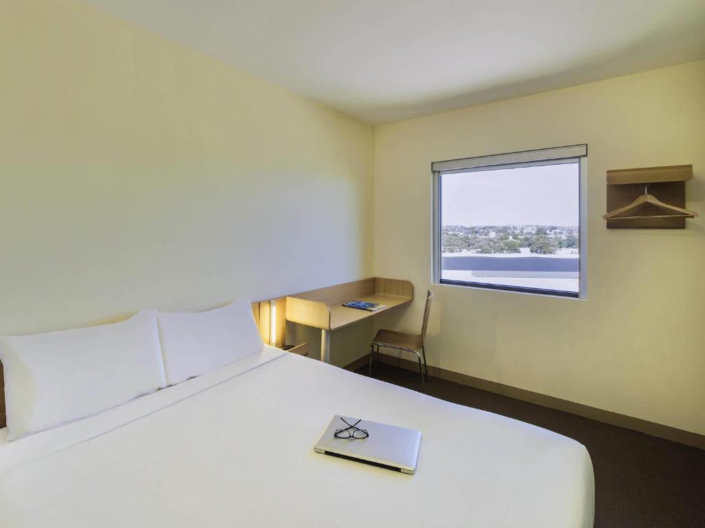 a bedroom with a large white bed with a window at ibis Budget Sydney Olympic Park in Sydney