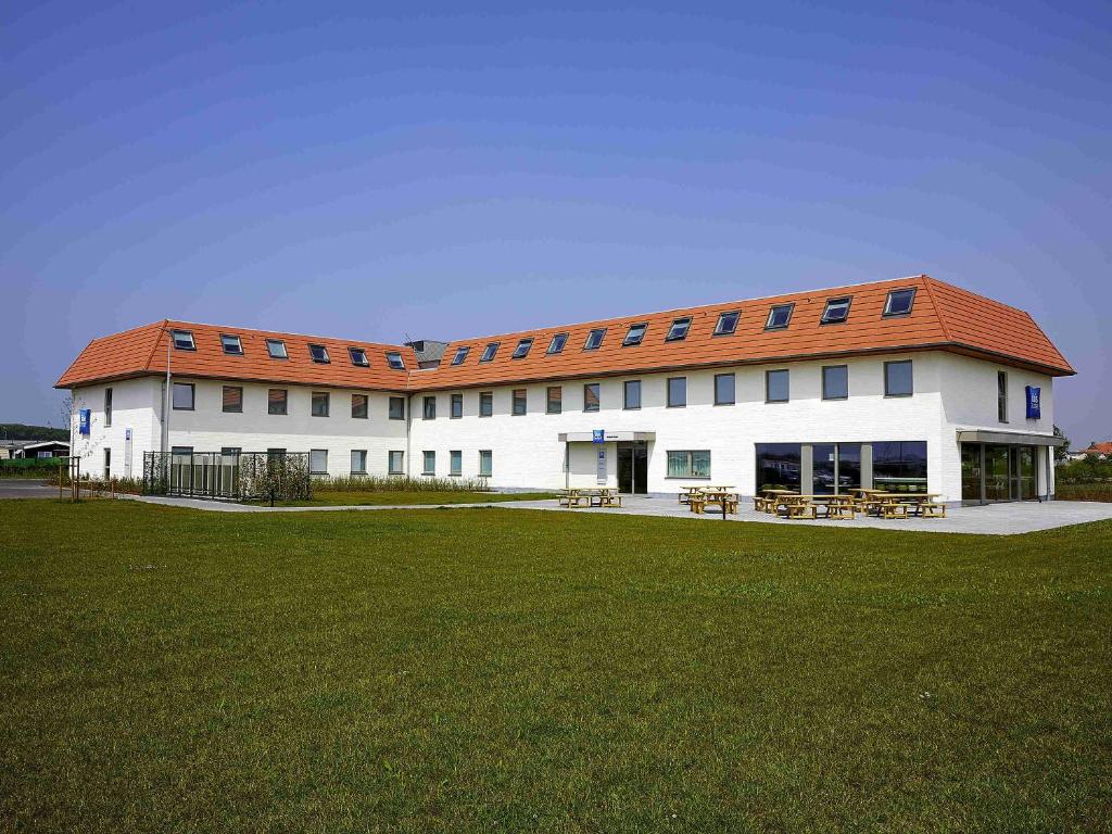 ein großes weißes Gebäude mit einem roten Dach in der Unterkunft ibis budget Oostende Airport in Ostende