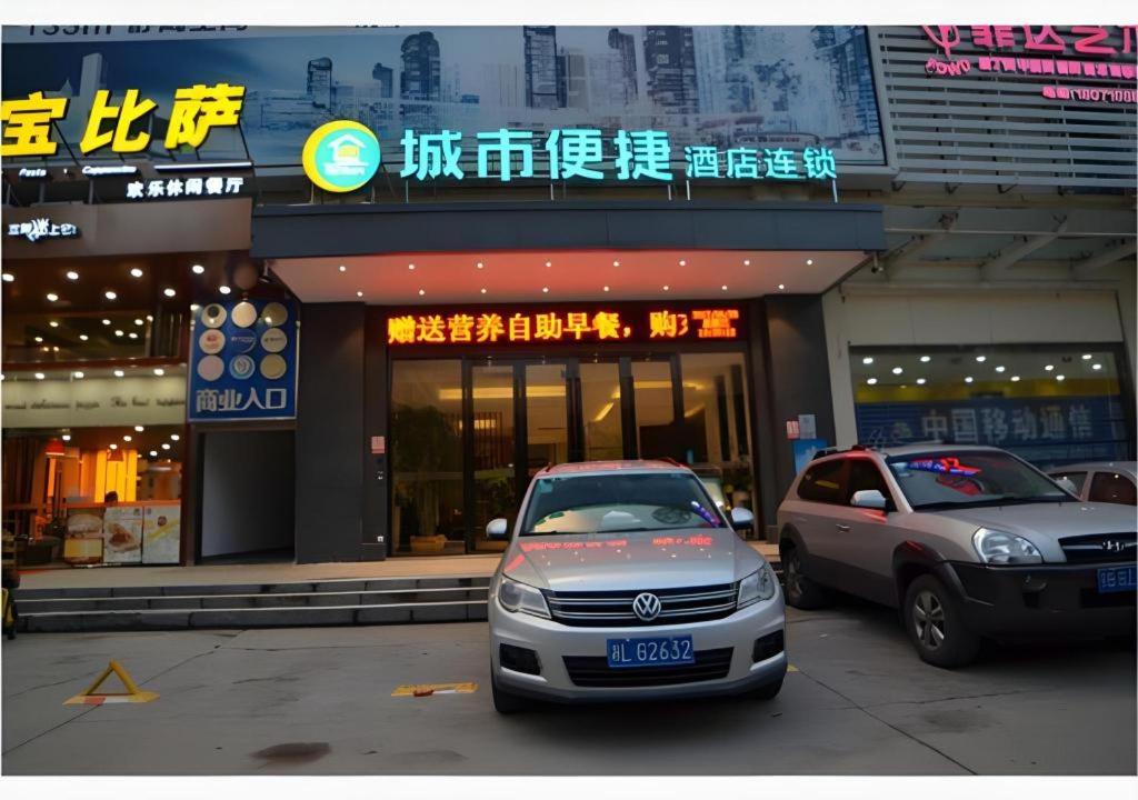 City Comfort Inn Wuhan East Lake Scenic Area Happy Valley في ووهان: سيارتان متوقفتان في موقف السيارات أمام مبنى