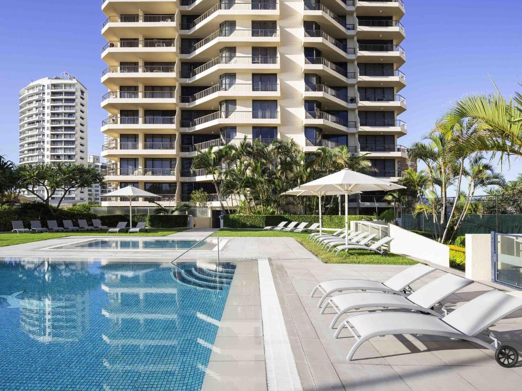 une piscine avec des chaises longues et un grand bâtiment dans l'établissement Paradise Centre Apartments, à Gold Coast