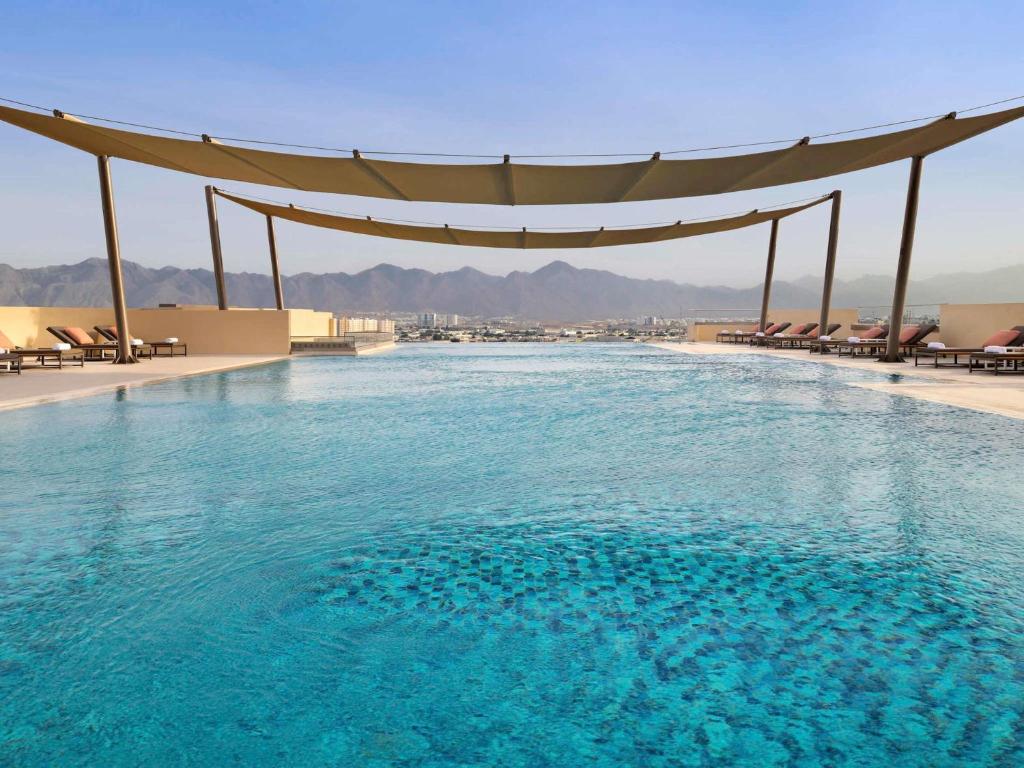 a swimming pool with a canopy over the water at Mövenpick Hotel & Apartments Ghala Muscat in Muscat