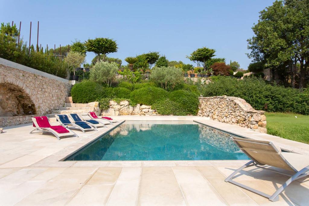 a swimming pool with lounge chairs next to a stone wall at Villa sur Golf Opio Valbonne in Opio