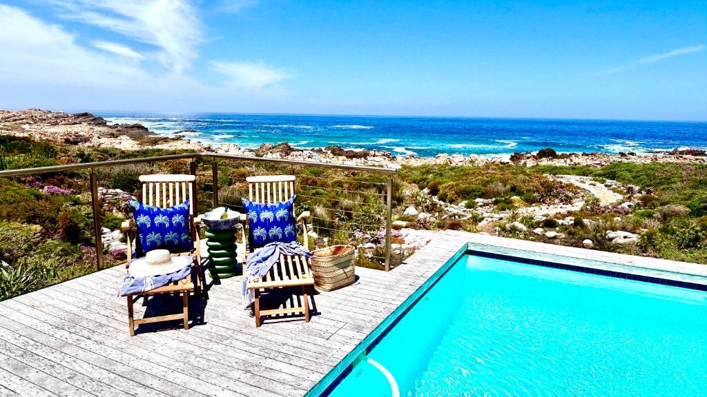 une piscine avec deux chaises et l'océan dans l'établissement Kalliste Boutique Stays, Misty Shores Cottage, à Bettyʼs Bay