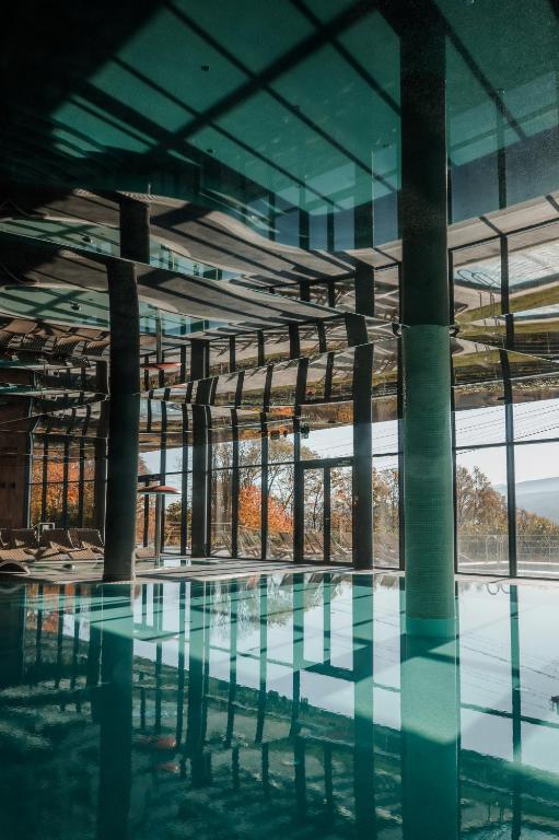 Sunlit indoor pool with tall glass windows and reflected pillars, serene panoramic view.
