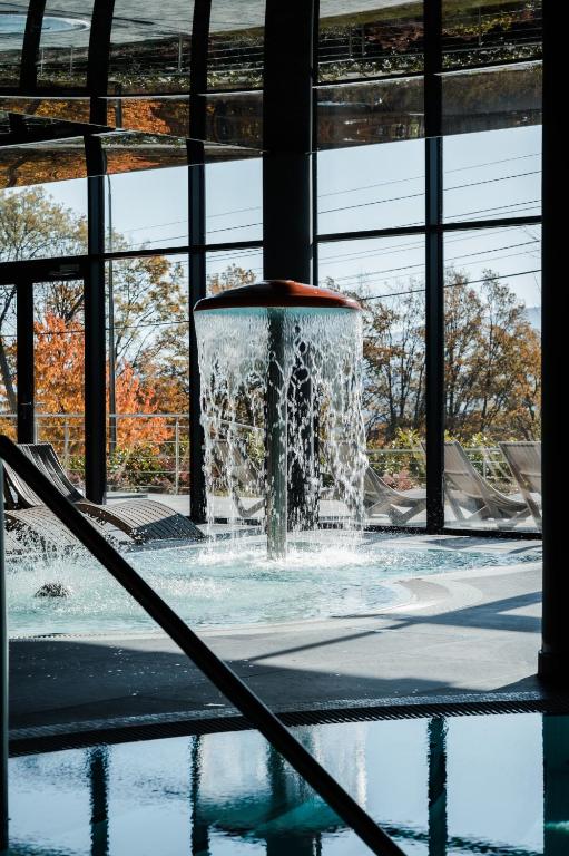 Mushroom-style water fountain cascading into pool by floor-to-ceiling windows and loungers.