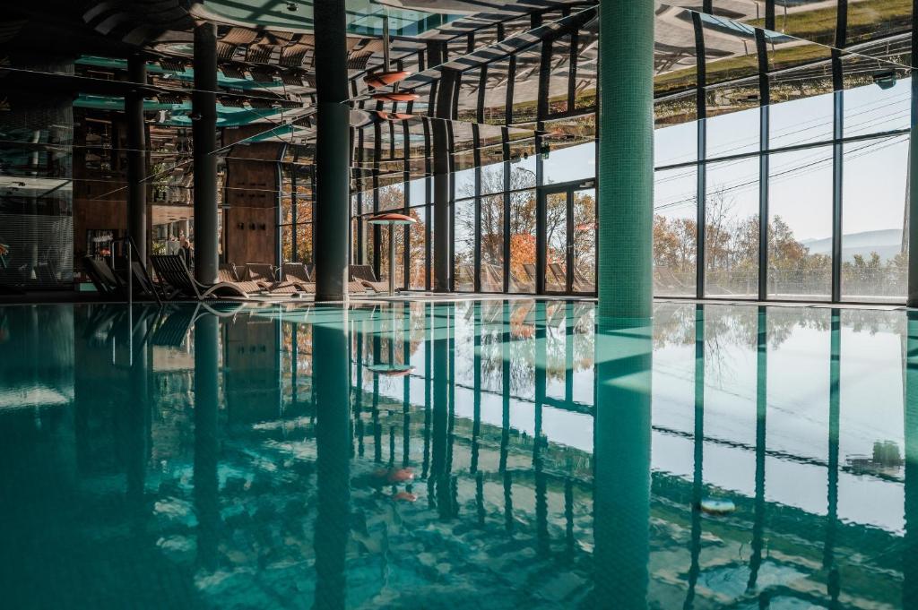 Wide indoor pool reflecting floor-to-ceiling windows and rows of loungers, tranquil atmosphere.