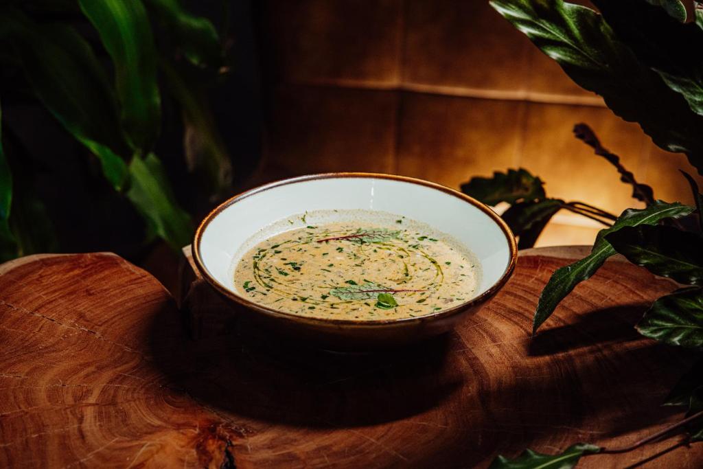 Creamy herb soup in a bowl with olive oil drizzle, served on wooden slab.
