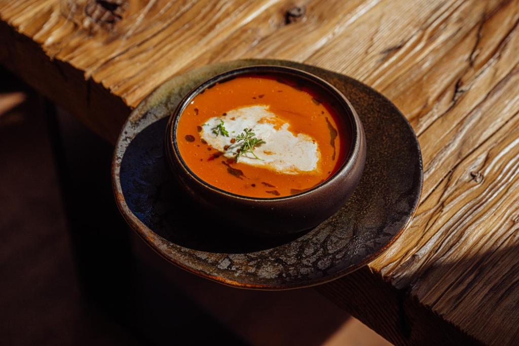 Warm tomato soup with cream swirl and small herb garnish served in a dark bowl on wooden table