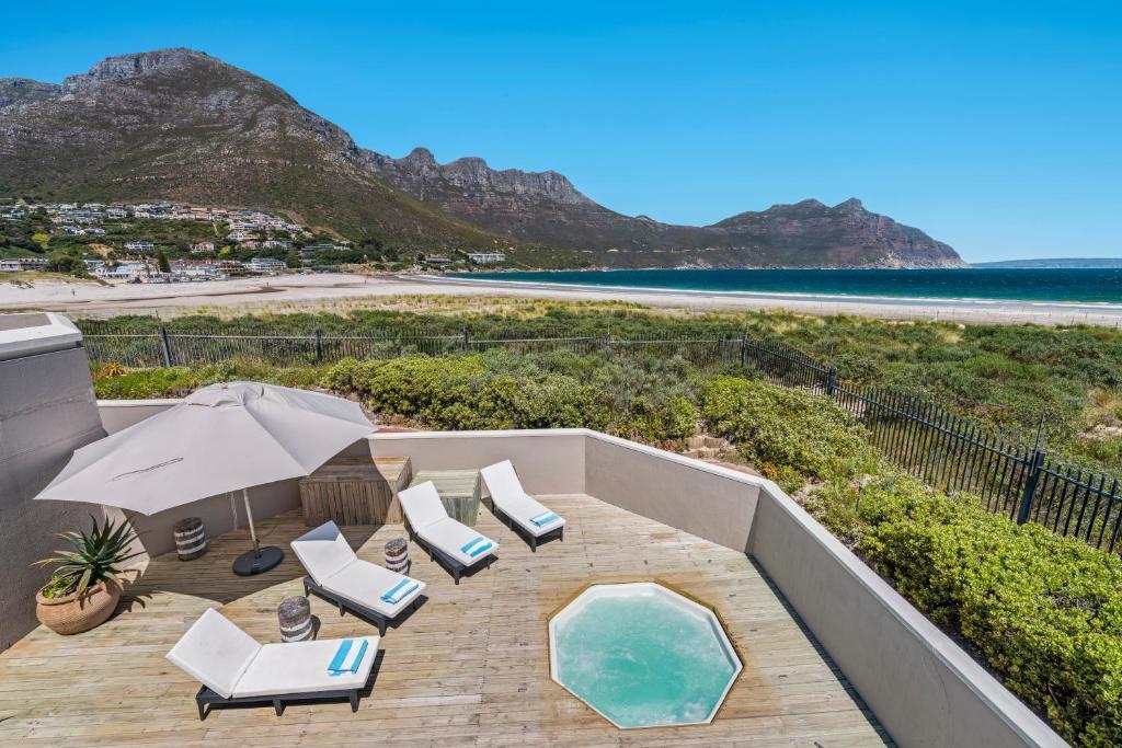 开普敦Pingu Beachhouse with Jacuzzi Hout Bay Cape Town的一个带椅子和遮阳伞的阳台以及一个游泳池。