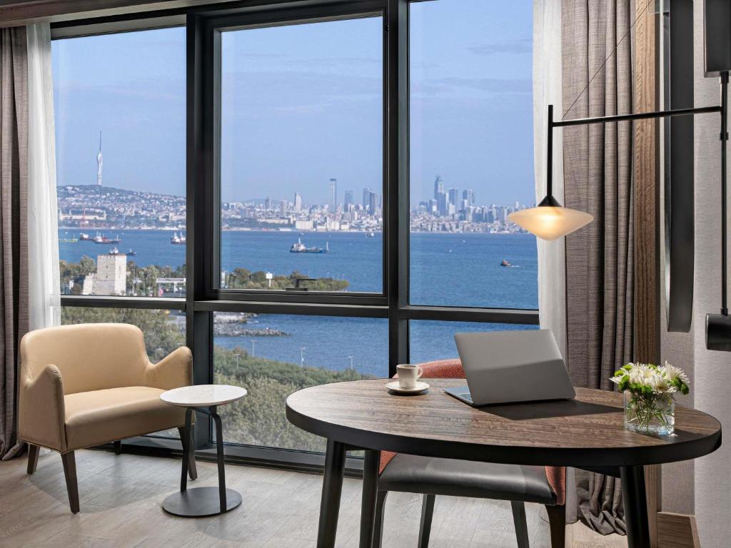 a room with a desk with a laptop and a large window at Mövenpick Hotel Istanbul Marmara Sea in Istanbul