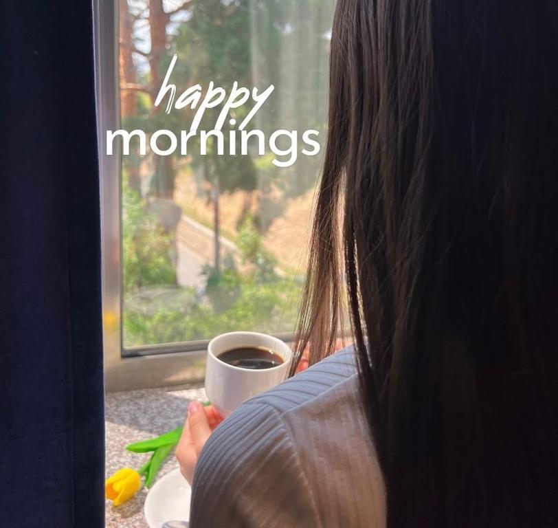 a woman holding a cup of coffee looking out a window at Prime Hotel Vayk at Lider Complex in Vaykʼ