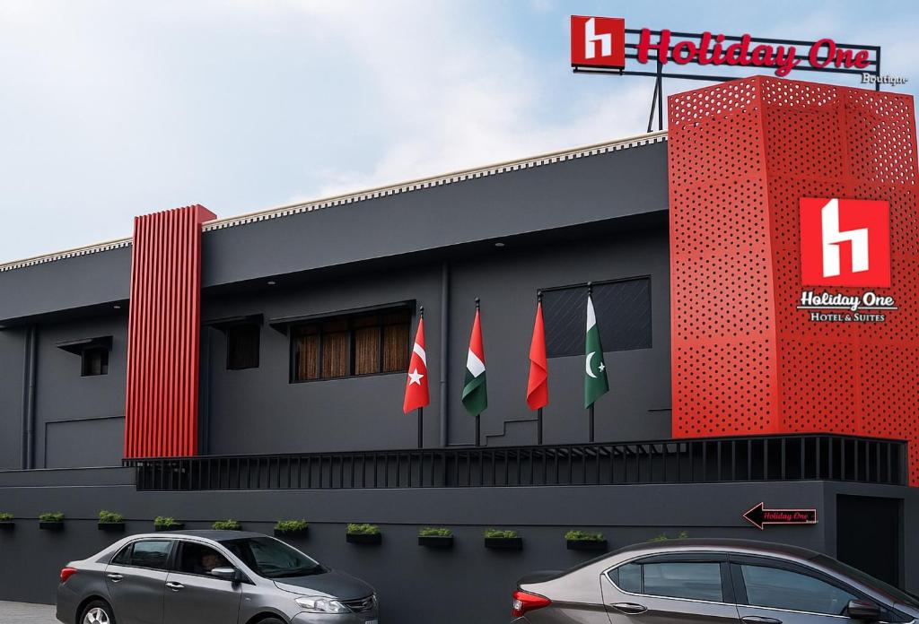 due auto parcheggiate di fronte a un edificio con bandiere di Holiday One Hotel & Suites a Karachi