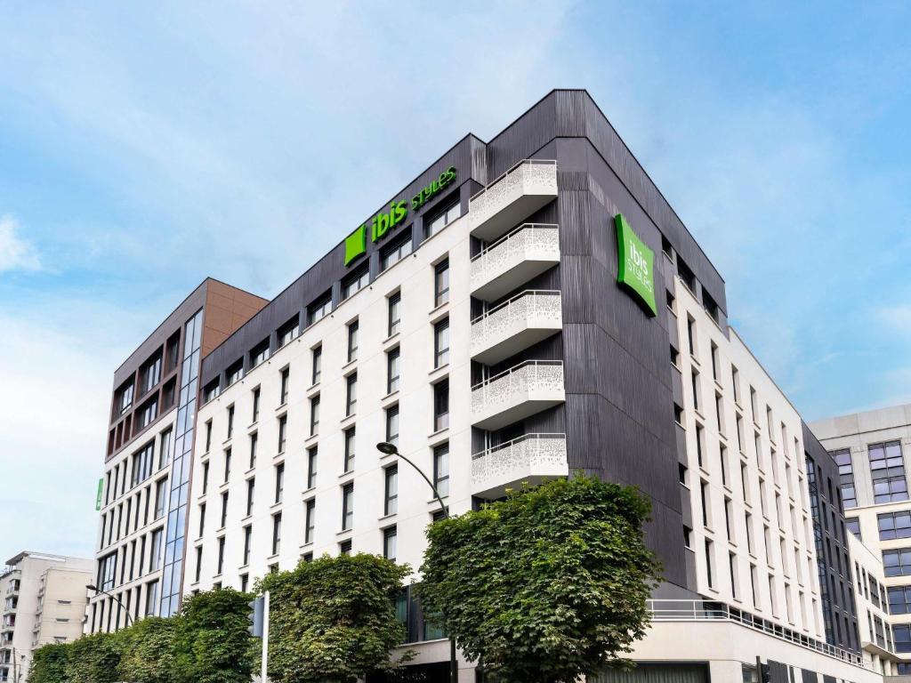 - un grand bâtiment avec un panneau vert dans l'établissement ibis Styles Paris Villejuif, à Villejuif