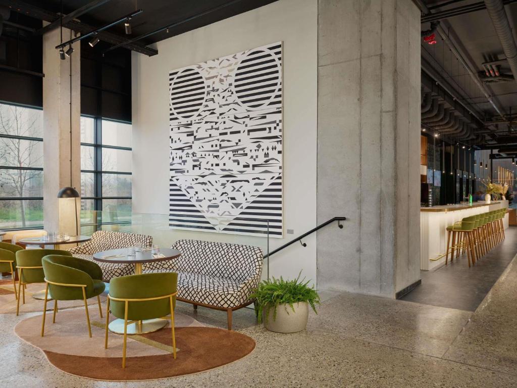 Lobby seating with green patterned sofas, gold wire chairs, abstract wall art, bar with wooden stools and large windows at Pullman Zagreb in Zagreb