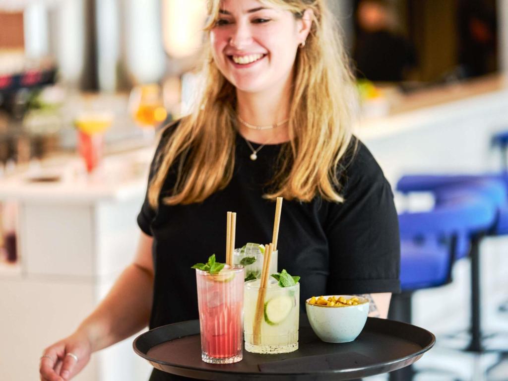 a woman holding a tray with two drinks on it at TRIBE Paris Clichy in Clichy