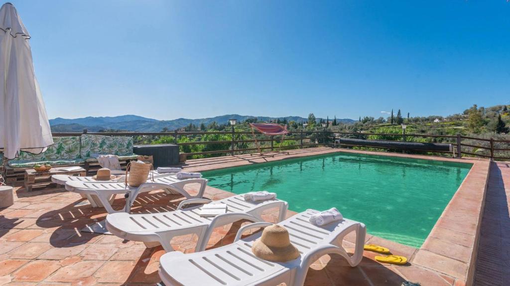 Una piscina con sillas blancas y una piscina. en Casa Perdi Riogordo by Ruralidays, en Ríogordo