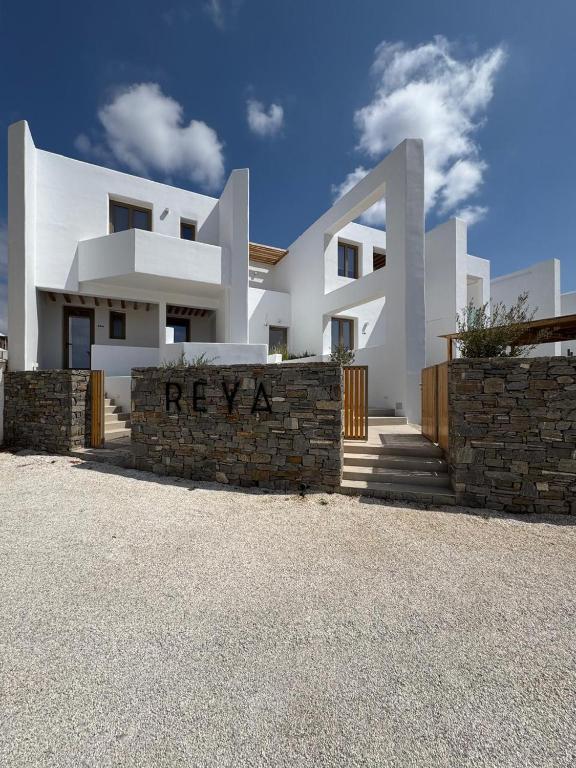 a white house with a stone retaining wall at REYA suites in Aliki