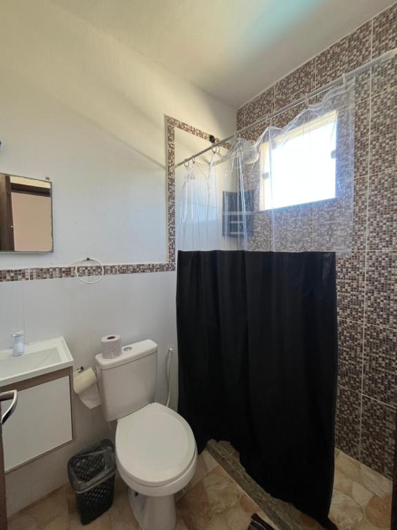 a bathroom with a toilet and a black shower curtain at Renascer Suites in Búzios