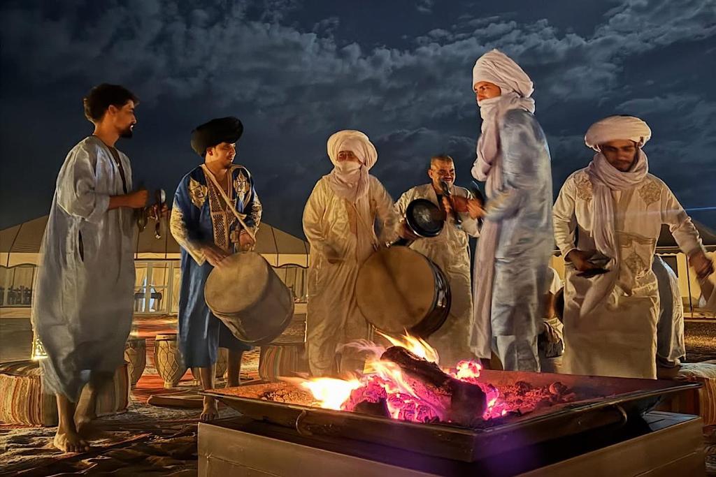 a group of people standing around a fire at Merzouga Twilight Camp in Merzouga