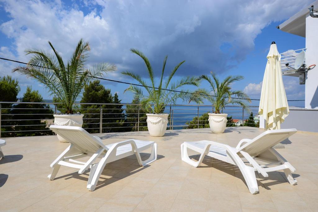 zwei weiße Stühle und ein Regenschirm auf einer Terrasse in der Unterkunft Apartmani Smiljanic in Starigrad-Paklenica