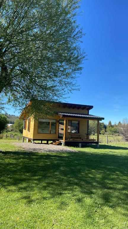 ein kleines Haus auf einem Feld mit einem Baum in der Unterkunft Cabaña Lilacho in Cholila