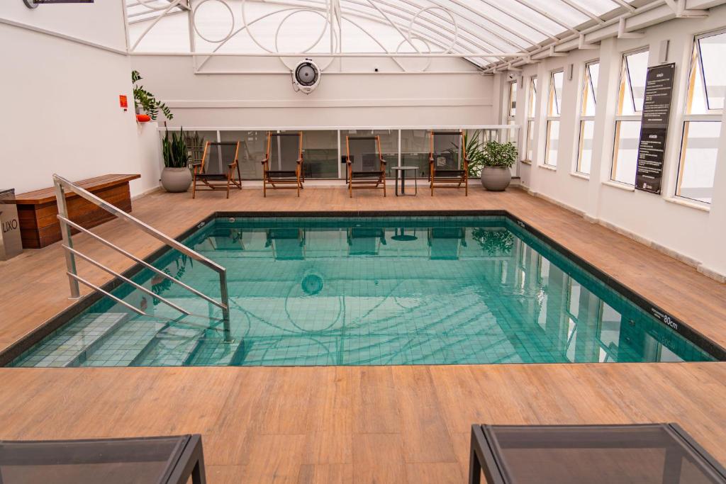 a swimming pool in a building with tables and chairs at Hotel Gumz in Balneário Camboriú