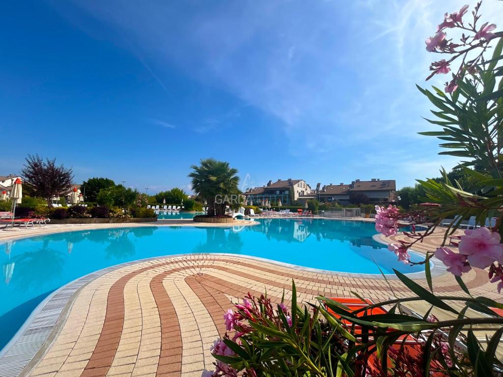 una grande piscina in un resort con fiori rosa di Platino Apartment - Jacuzzi privata, tre Piscine residenziali ed un bar a 200m dal Lago a Desenzano del Garda