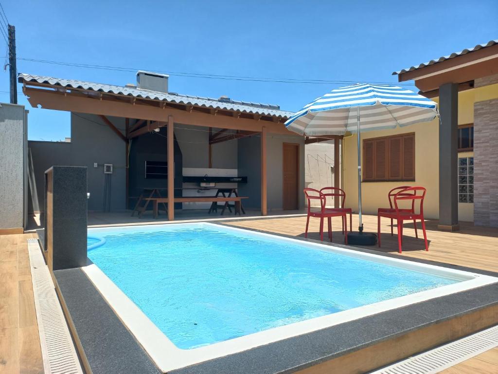 a swimming pool with chairs and an umbrella next to a house at Casa Com Quatro Dormitórios, Pertinho Do Mar Em Capão Da Canoa in Capão da Canoa