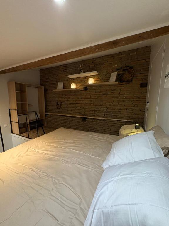 Cette chambre comprend un grand lit blanc et un mur en briques. dans l'établissement Duplex Haut de Gamme Centre Montauban, à Montauban