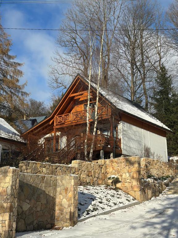 a log cabin in the snow with a stone wall at Dom drewniany z sauną i jacuzzi w Szklarskiej Porębie in Szklarska Poręba