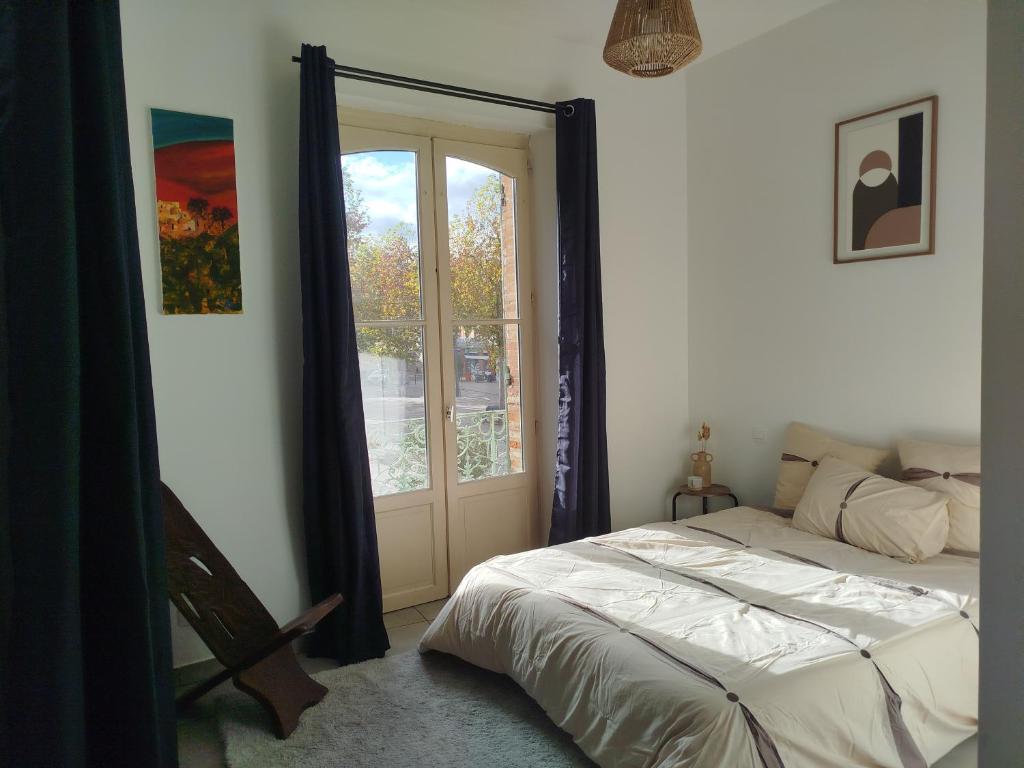 une chambre avec un lit et une grande fenêtre dans l'établissement Charmant appart avec balcon donnant sur place de la mairie, à Castelsarrasin