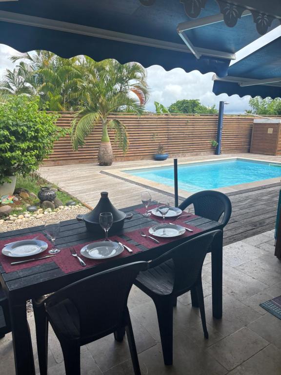 ein Esstisch mit Tellern und Weingläsern und ein Pool in der Unterkunft Tropikaz in Le Diamant