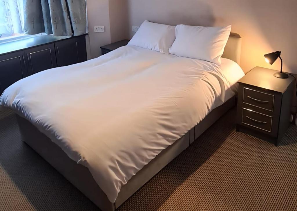 ein Bett mit weißer Bettwäsche und einer Lampe auf einem Nachttisch in der Unterkunft 1BR London Home Private Bathroom and Kitchen 10min to Heathrow in Cranford