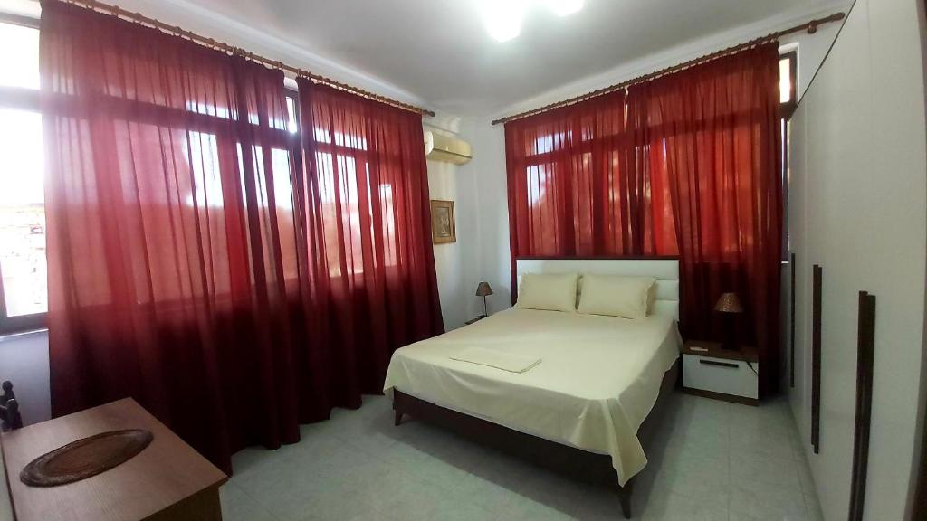 1 dormitorio con cortinas rojas y 1 cama blanca en Central Apartments Shoshi, en Tirana
