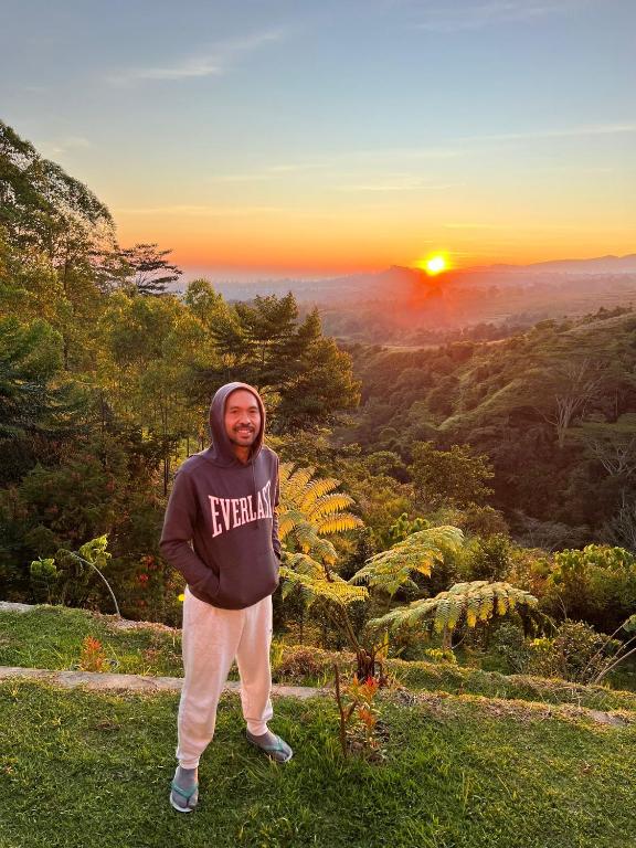 a man standing on a hill with the sunset in the background at Ruteng Glamping & Campsite in Ruteng
