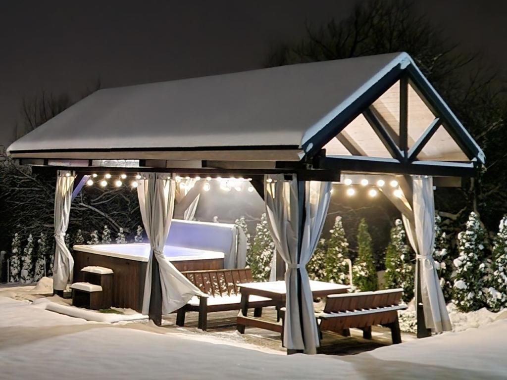 a gazebo with benches and lights in the snow at Domek na Folwarku z jacuzzi in Tarnawa Dolna