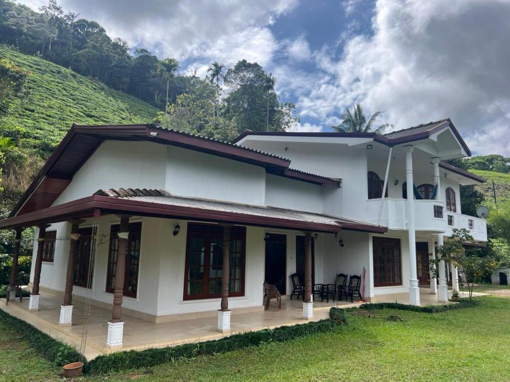 a white house with a green hill in the background at Upton Estate Homestay in Deniyaya