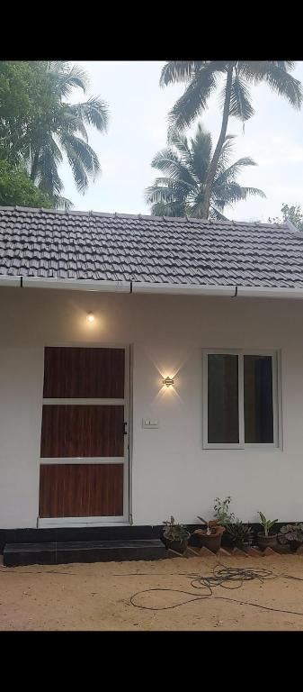 a white house with a door and a palm tree at Katadi beach coral cottage in Thanniyam