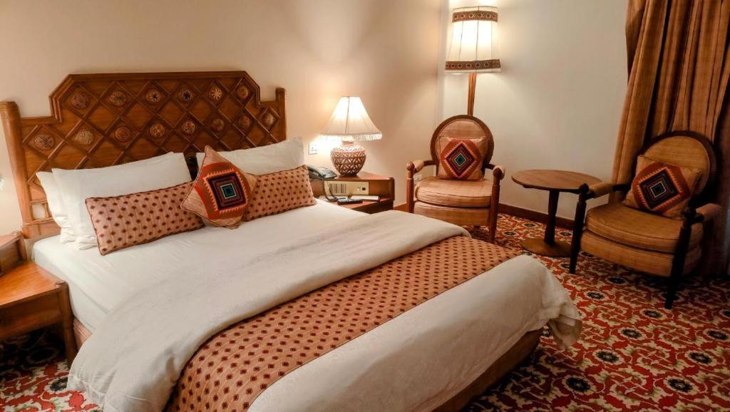 Una habitación de hotel con una cama grande y dos sillas. en Sarena Hotel, en Quetta