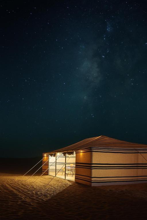 Un pequeño edificio en la arena por la noche. en Aurora desert camp, en Badīyah