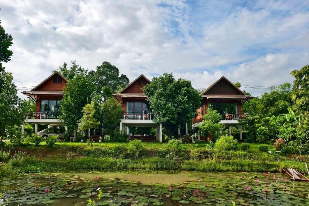 une maison avec un étang devant dans l'établissement บ้านกลางเกาะ รีสอร์ท, à Uthai Thani