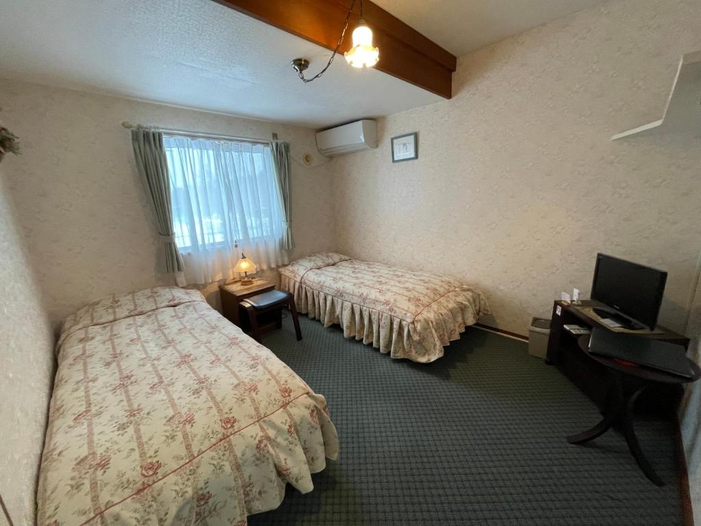 une chambre d'hôtel avec deux lits et un bureau avec un ordinateur dans l'établissement ペンションあけまの森, à Daisen