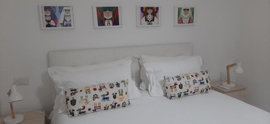 ein weißes Bett mit zwei Kissen und Bildern an der Wand in der Unterkunft CIVICO 16A - Apartment - with private parking in Quartu SantʼElena