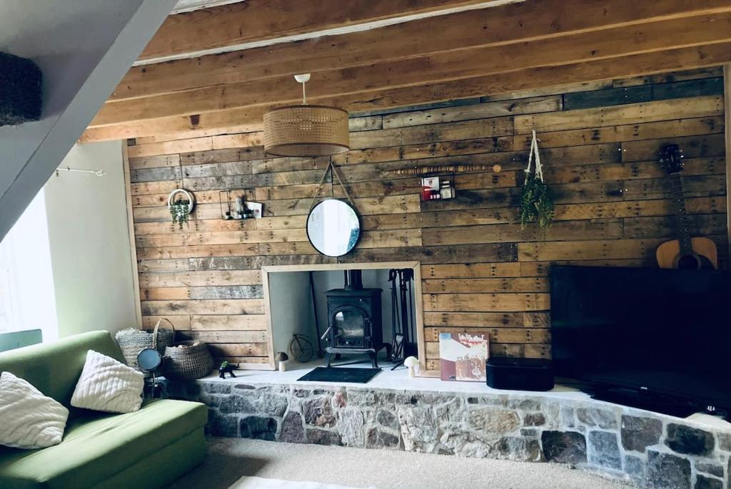 a living room with a wooden wall with a fireplace at Nant caer Efail Cottage - Stream by the forge in Pen-y-cae