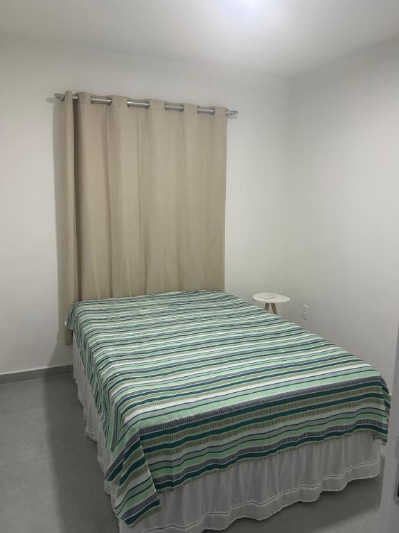 a bed in a white room with a striped blanket at Apto com dois quartos com cama e ar in Juazeiro do Norte