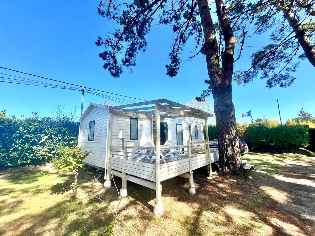 une petite maison blanche assise à côté d'un arbre dans l'établissement Mobile Home Camping Paradis, à Trédrez