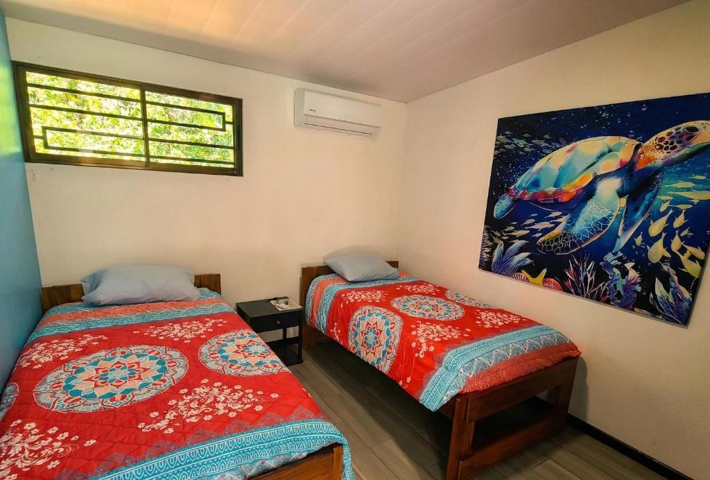 Un dormitorio con dos camas y un cuadro en la pared. en Pura Vida - Villa Elenita, en Parrita