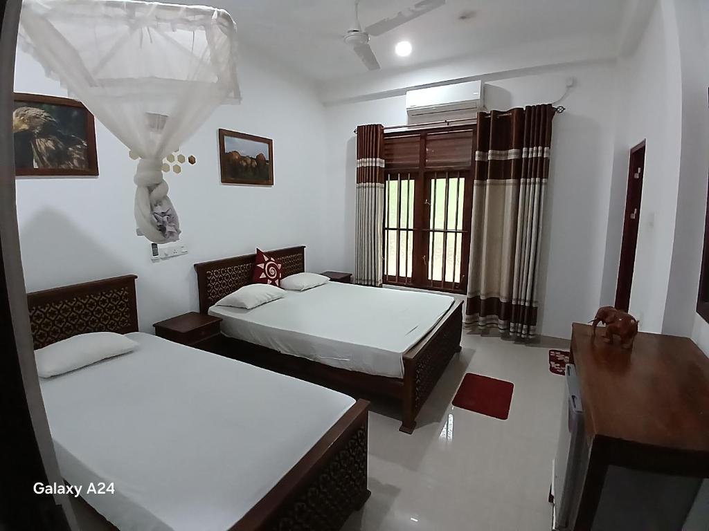 a bedroom with two beds and a table and a window at Walawa cottage udawalawe in Udawalawe